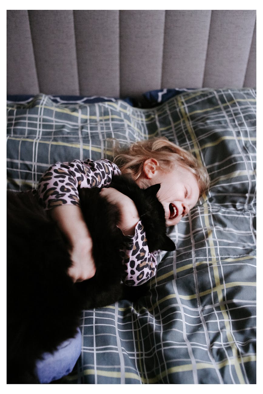 Happy child laughing while hugging a black cat on a bed indoors.